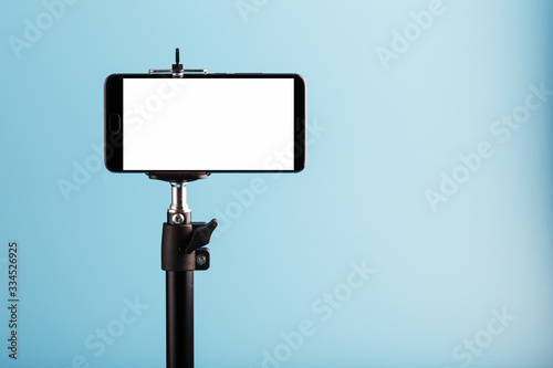 Mobile phone on a tripod with a clear white display for image and text, blue isolated background. photo