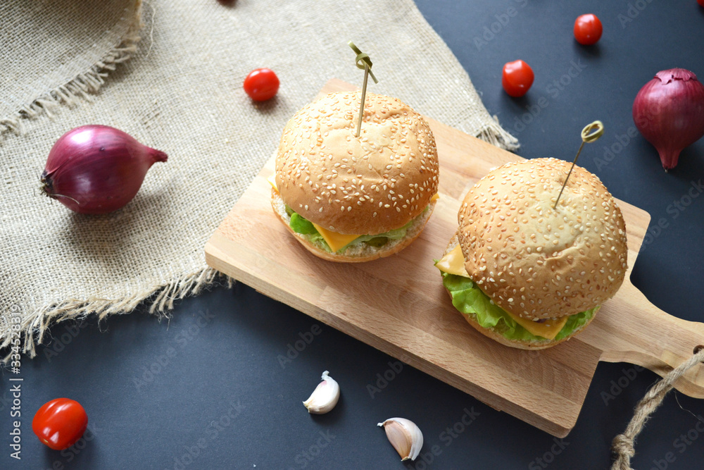 homemade hamburgers on a wooden board with cherry tomatoes, red onions and pickles on a black background