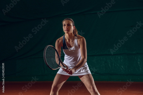Young caucasian professional sportswoman playing tennis on sport court background. Training, practicing in motion, action. Power and energy. Movement, ad, sport, healthy lifestyle concept. Front view. © master1305