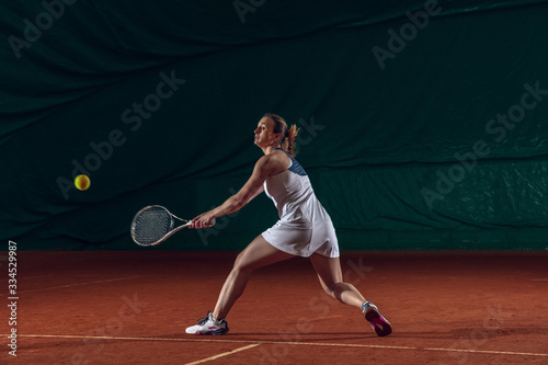 Young caucasian professional sportswoman playing tennis on sport court background. Training, practicing in motion, action. Power and energy. Movement, ad, sport, healthy lifestyle concept. Front view. © master1305