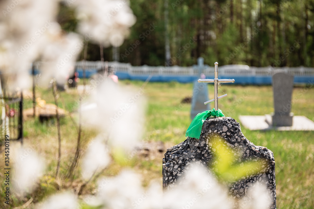 Naklejka premium Ancient grave with tombstone and cross on top. Spring day commemoration of the dead. Prayer for the souls of our relatives, friends, relatives and ancestors. A branch of blooming cherry.