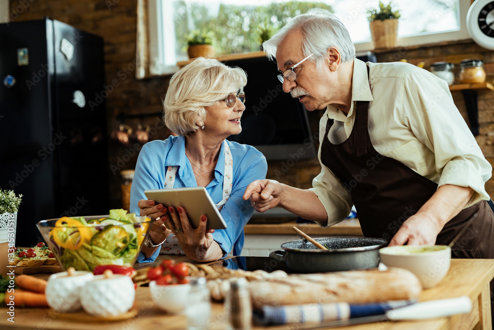 Mature couple using digital tablet while cooking together in the kitchen. Mature couple using digital tablet while cooking together in the kitchen.