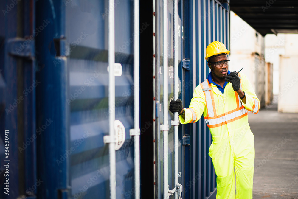 Adult African american men worker Check and control loading freight Containers by use radio at commercial shipping dock felling serious. Cargo freight ship for import export concept Adult African american men worker Check and control loading freight Containers by use radio at commercial shipping dock felling serious. Cargo freight ship for import export concept