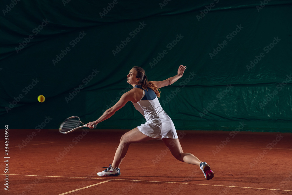 Young caucasian professional sportswoman playing tennis on sport court background. Training, practicing in motion, action. Power and energy. Movement, ad, sport, healthy lifestyle concept. Front view.