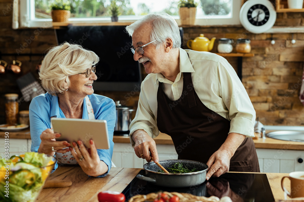 Happy senior couple talking while cooking and using touchpad in the kitchen. Happy senior couple talking while cooking and using touchpad in the kitchen.