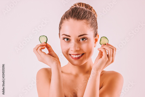 Young happy woman beauty model holding cucumber slices in hands and smiling. Beautiful girl with pefrect clean face skin posing with cucumbers isolated on background. Beauty pampering, cosmetology photo