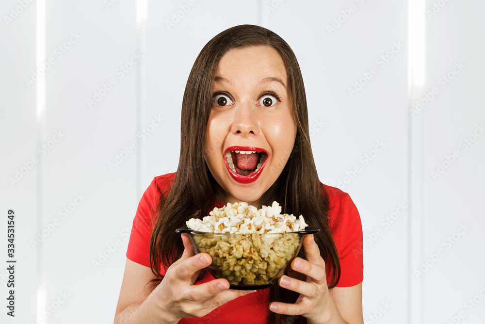 Young pretty girl with opened mouth and wide eyes holds glass bowl with popcorn Young pretty girl with opened mouth and wide eyes holds glass bowl with popcorn
