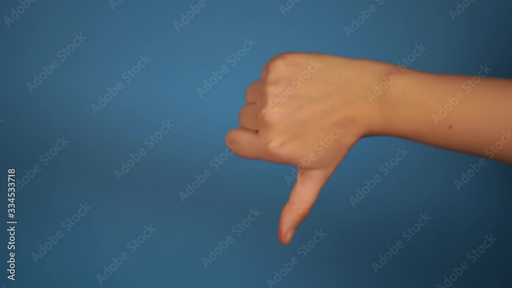 Woman's hand showing thumb down on blue background. Close-up of hand showing gesture of disapproval. The concept of dislike. Woman's hand showing thumb down on blue background. Close-up of hand showing gesture of disapproval. The concept of dislike.
