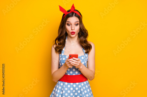Portrait of astonished girl blogger use her cellphone read social network information impressed scream wow omg wear polka-dot outfit isolated over bright shine color background