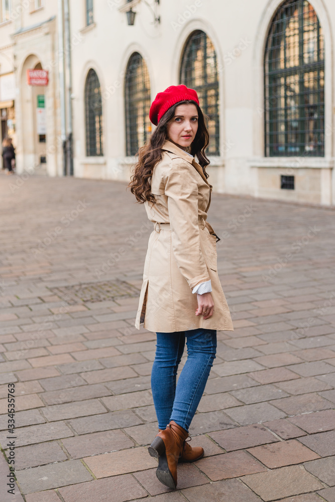 Naklejka premium Beautiful young woman at city street. Happy tourist girl walking outdoors. Spring full body fashion portrait of pretty brunette female posing in old town.