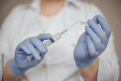 doctor in white coat and gloves holds a syringe with a vaccine