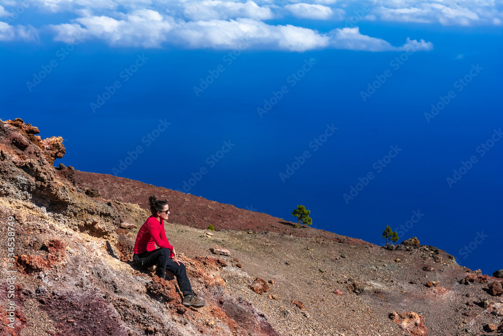 Young woman smiling with satisfaction,  sitting on volcanic rock and relaxing after hike. Outdoor Lifestyle Photo. La Palma, Canary Islands, Spain.