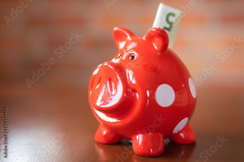 Red piggy bank with a 5 euro banknote inserted.