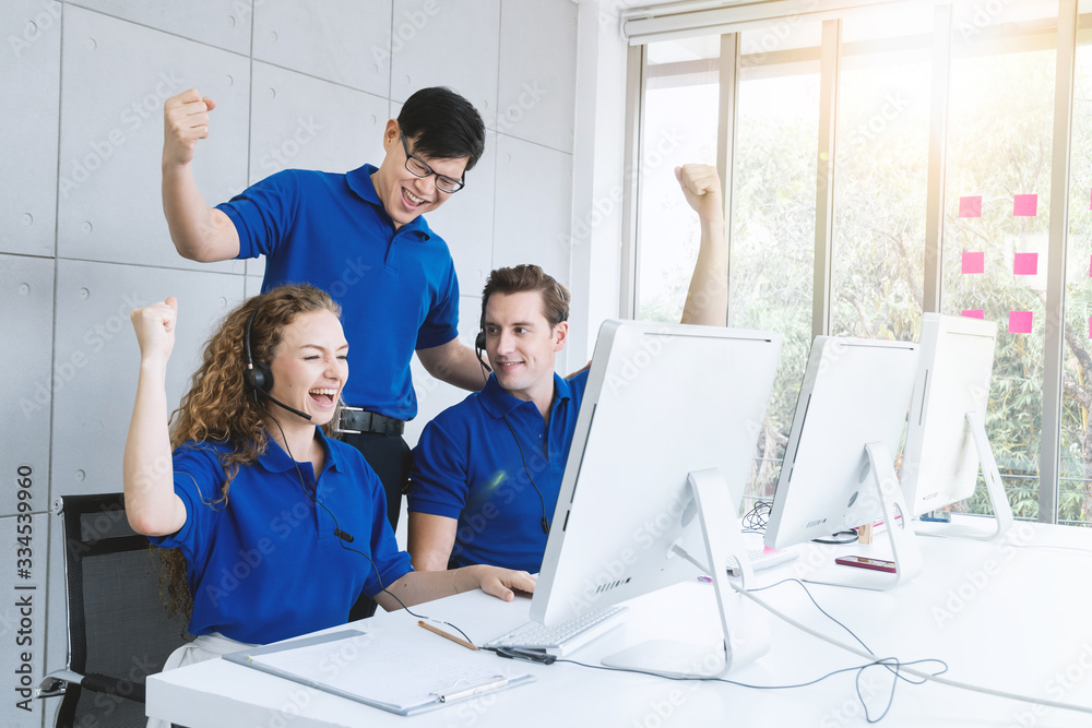 Cheerful customer service team and manager had arms up to celebrating our success at desk with computer and headset in modern office.