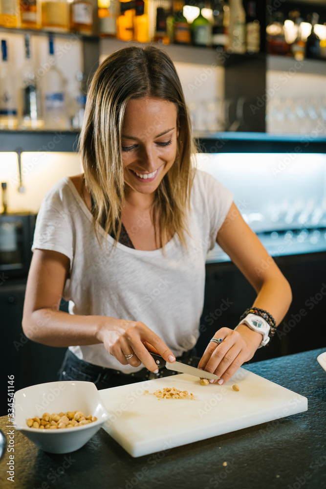 Fototapeta premium Young woman chef chopping peanuts on a table to prepare some delicious asian noodles in a modern restaurant