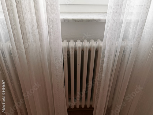 The central heating radiator is covered with light white curtains