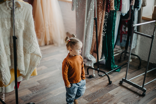 little pretty girl walking in dressing room amidst large selection of clothes and women's dresses