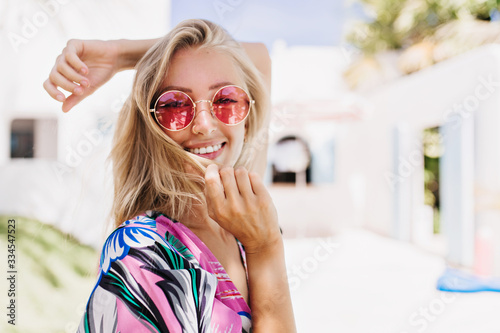 Ecstatic girl wears pink sunglasses expressing happiness in summer day. Outdoor photo of wonderful tanned woman posing with pretty smile in sunny morning.