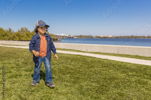 An urban toddler dressed in denim walks by the waterfront. On a typical sunny spring day is the perfect setting to go for a walk along the inter-coastal sidewalk.