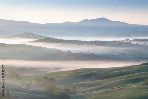 Beautiful colors of green spring panorama landscape of Tuscany. Most popular place in Italy. Green fields and blue sky and Cypress tree scenic road near Siena. Amazing foggy morning with sunshine