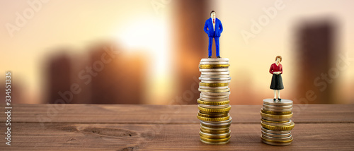 фотографія Miniature people: a businessman and a businesswoman standing on stack of coins with some coins laying behind them, city backround