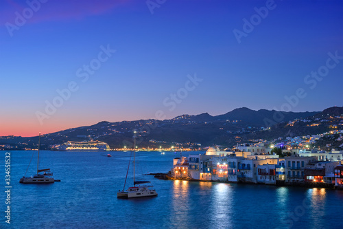 Sunset in Mykonos island, Greece with yachts in the harbor and colorful waterfront houses of Little Venice romantic spot on sunset and cruise ship illuminated in night. Mykonos townd, Greece