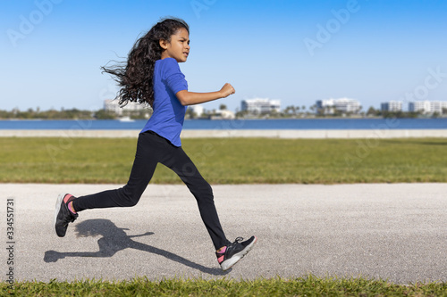 The young female runner looks at a distance as she begins to slow down at the waterfront park.She was captured in midair  running with a defined shadow clearly outlined on the pavement.