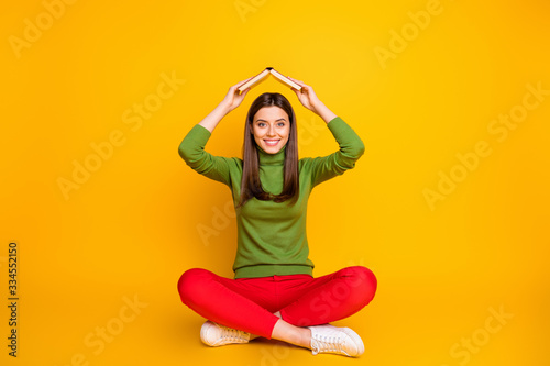Photo of beautiful funny lady sit floor holding school literature book under head cheery childish mood wear casual green pullover red trousers isolated yellow color background © deagreez