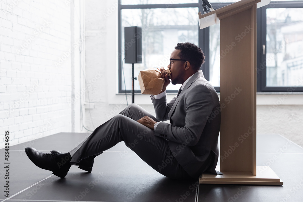 nervous african american speaker breathing with paper bag and having panic attack during business conference in office