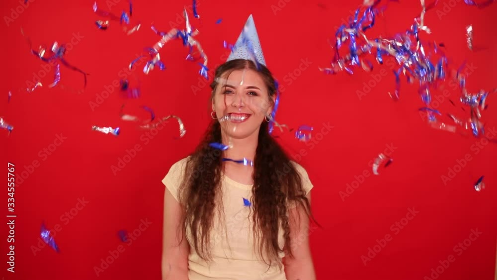 Attractive girl in a festive cap wishes a happy birthday and throws confetti. Isolated on a red background. Attractive girl in a festive cap wishes a happy birthday and throws confetti. Isolated on a red background.