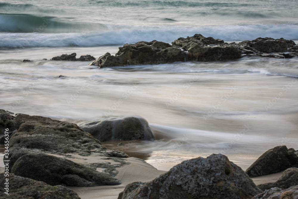 Long Exposure Shot of Rocks on a Beach with Ocean Waves during Daylight