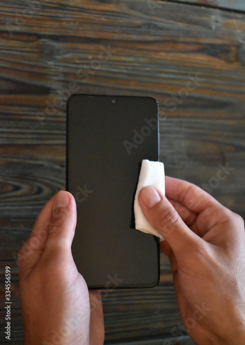 Manos limpiando y desinfectando un celular negro contra virus y bacterias con una toallita húmeda	 photo