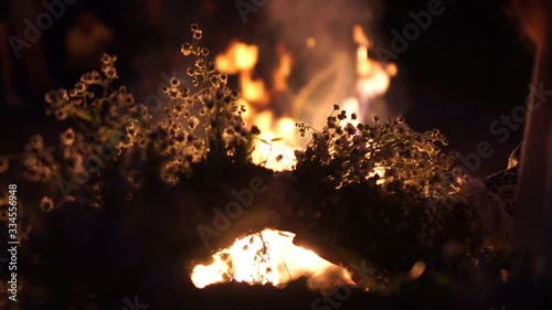 Girl holding a wreath of fresh flowers in her hands, in the background burning fire