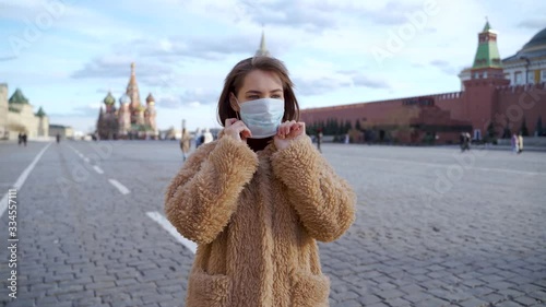 COVID-19: young woman is putting on medical face mask on the Red Square in Moscow, protection from coronavirus in Moscow