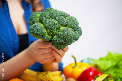 Woman at a table holding broccoli on a background of fruit and vegetables