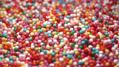 Colorful sprinkles sugar candy fall on table. multi-colored dragee fall into anothe multicolored balls. Red blue green yellow white orange.