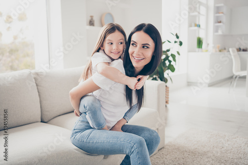 Photo of candid pretty lovely mother hold her cute little girl kid play game piggyback sit divan in modern light room photo