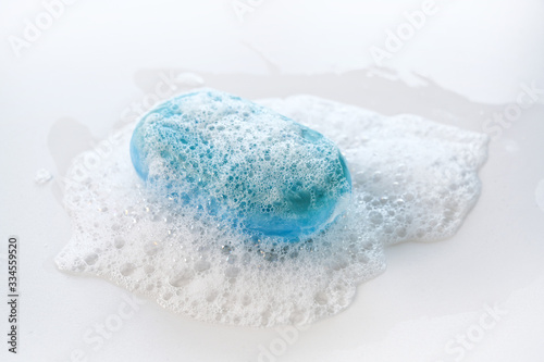 bar of blue soap with a lot of foam and bubbles on a white background, health care and hygiene concept against coronavirus infection, copy space