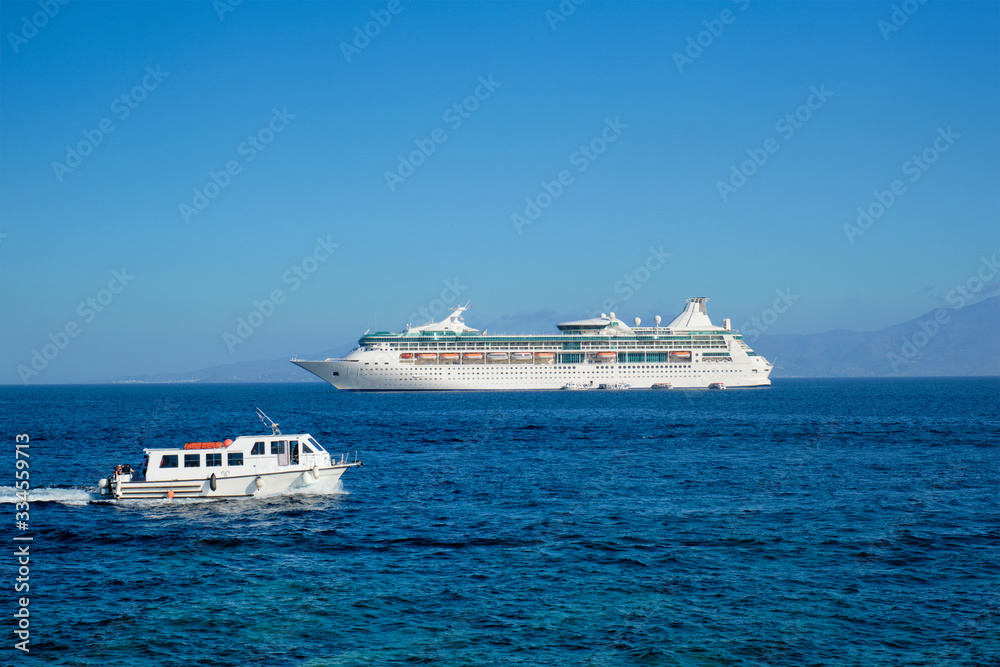 Boat and cruise liner is Aegean sea on beautiful summer day. Chora, Mykonos island, Greece