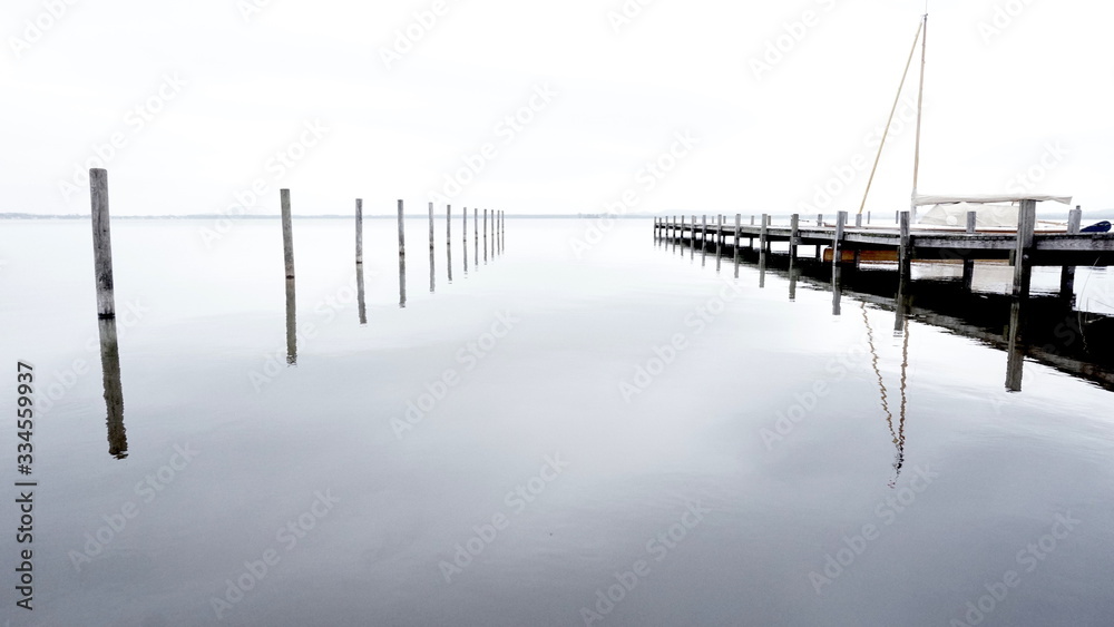 Minimalistic Pier Background with Wooden Pillars or stakes reaching out of calm Sea water with docking reflection in lake