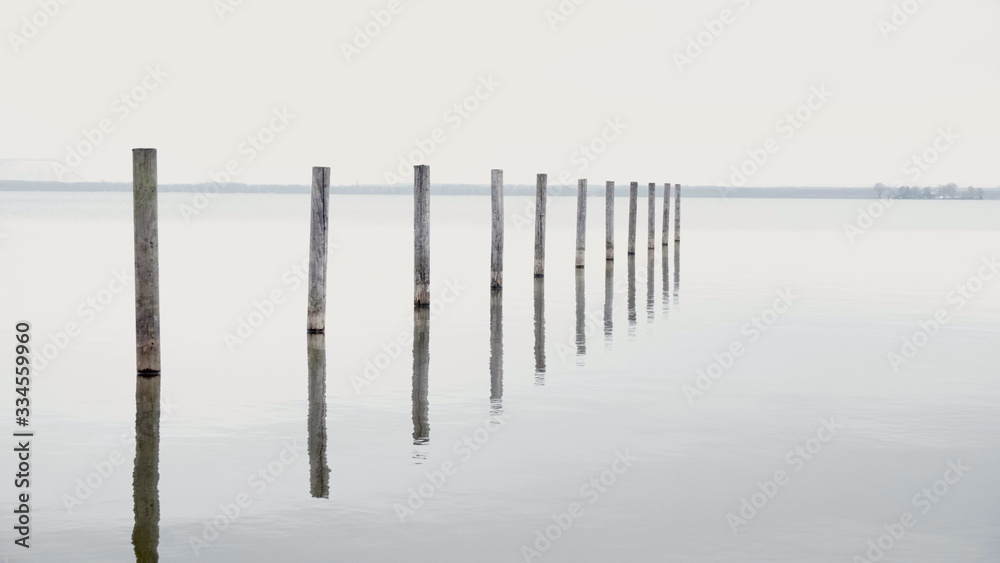 Minimalistic Pier Background with Wooden Pillars or stakes reaching out of calm Sea water with docking reflection in lake