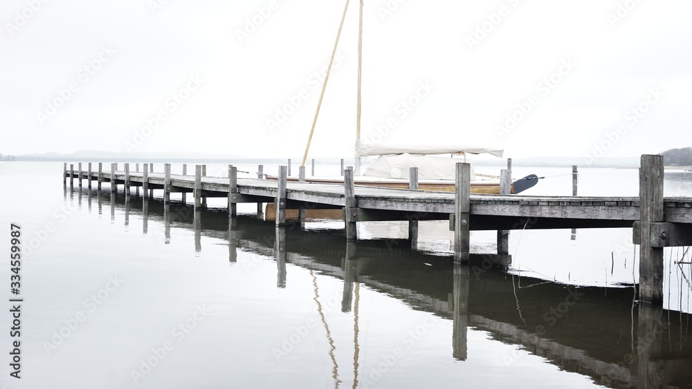 Sailing Boat docking on a pier at a lake with calm water reflection on a grey and cloudy day