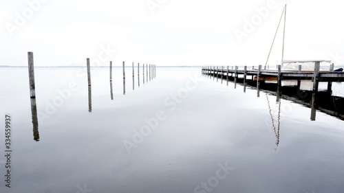 Obraz na płótnie Minimalistic Pier Background with Wooden Pillars or stakes reaching out of calm Sea water with docking reflection in lake w salonie