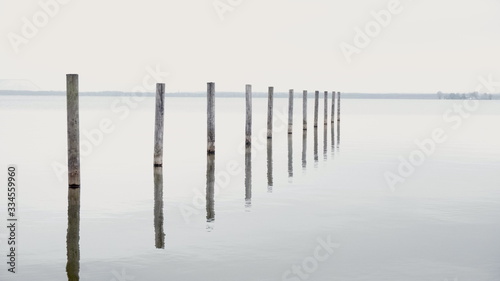 Obraz na płótnie Minimalistic Pier Background with Wooden Pillars or stakes reaching out of calm Sea water with docking reflection in lake w salonie
