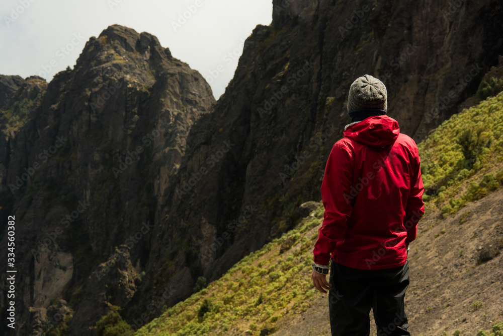 climber man standing on the mountain looking at the horizon dressed in a red sweater and in the background the peaks of a mountain, equator climber man standing on the mountain looking at the horizon dressed in a red sweater and in the background the peaks of a mountain, equator