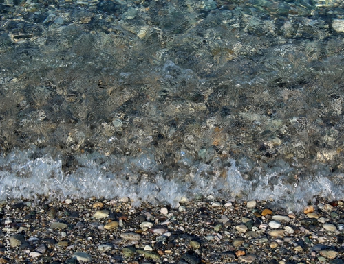Small wavelets breaking on the seashore covered by pebbles and cobbles