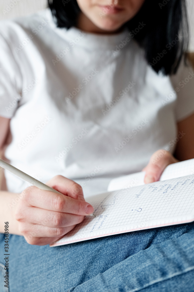 A girl in jeans and a white T-shirt writes with a pen in a notebook, closeup. Home or distance learning concept, Work from home, freelance A girl in jeans and a white T-shirt writes with a pen in a notebook, closeup. Home or distance learning concept, Work from home, freelance