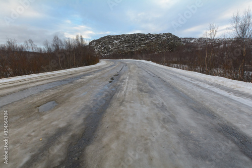 The dirt road is covered with ice .The sky is covered with clouds.