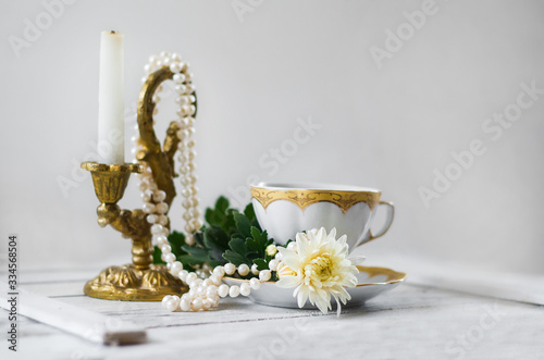 white cup of tea standing near the candle and pearls 