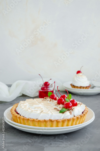 Tart with cherry filling and Italian meringue with a cocktail cherry, chocolate and mint on top on a white plate on a dark concrete background. Cherry pie. Sweet Food background. Vertical, Copy space.